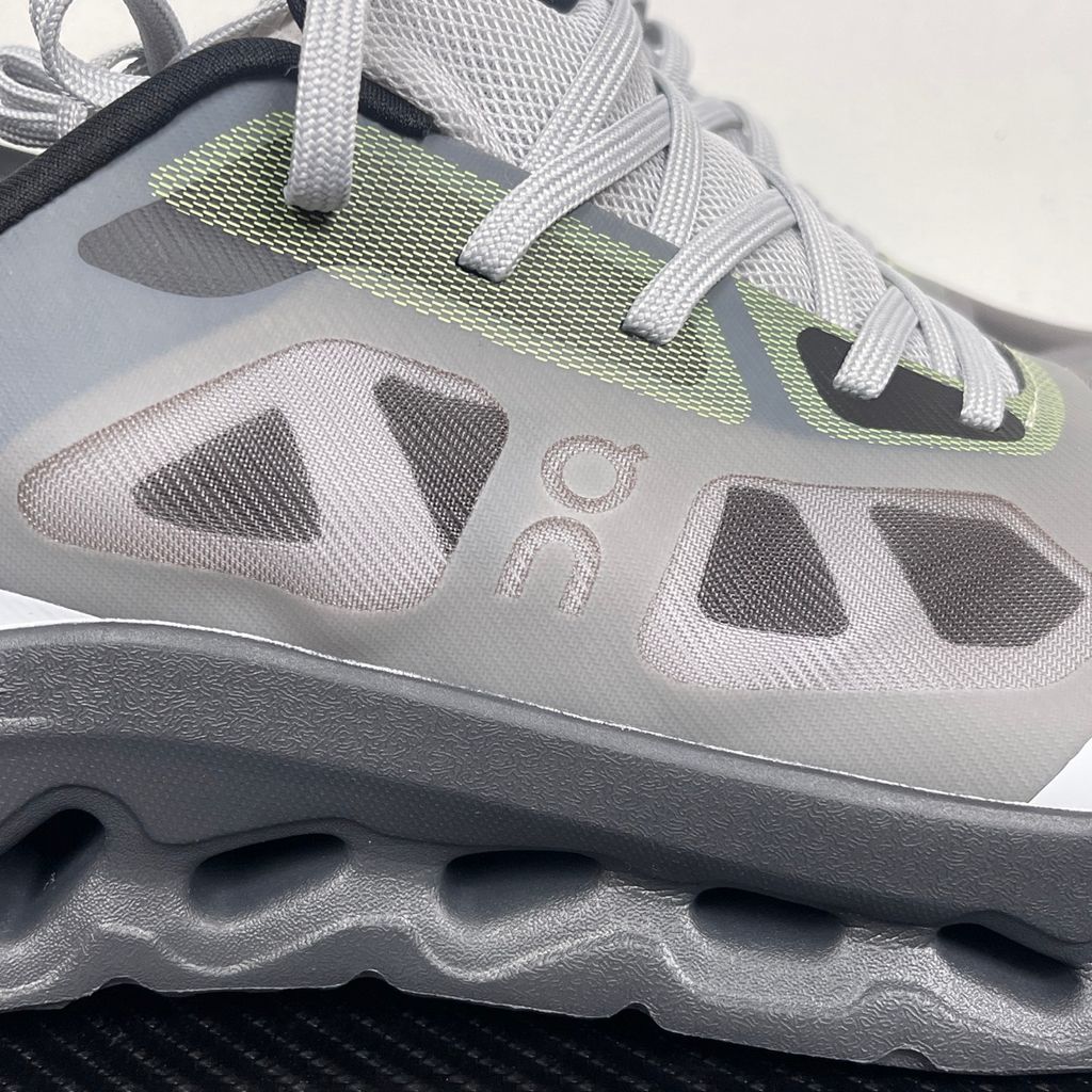 Side profile of the On Running Cloudtilt Remix sneaker, showcasing the mixed-material upper in dark grey and white with subtle green mesh undertones, quick-adjust speed lacing, and the distinctive dark grey CloudTec Phase® collapsing midsole.