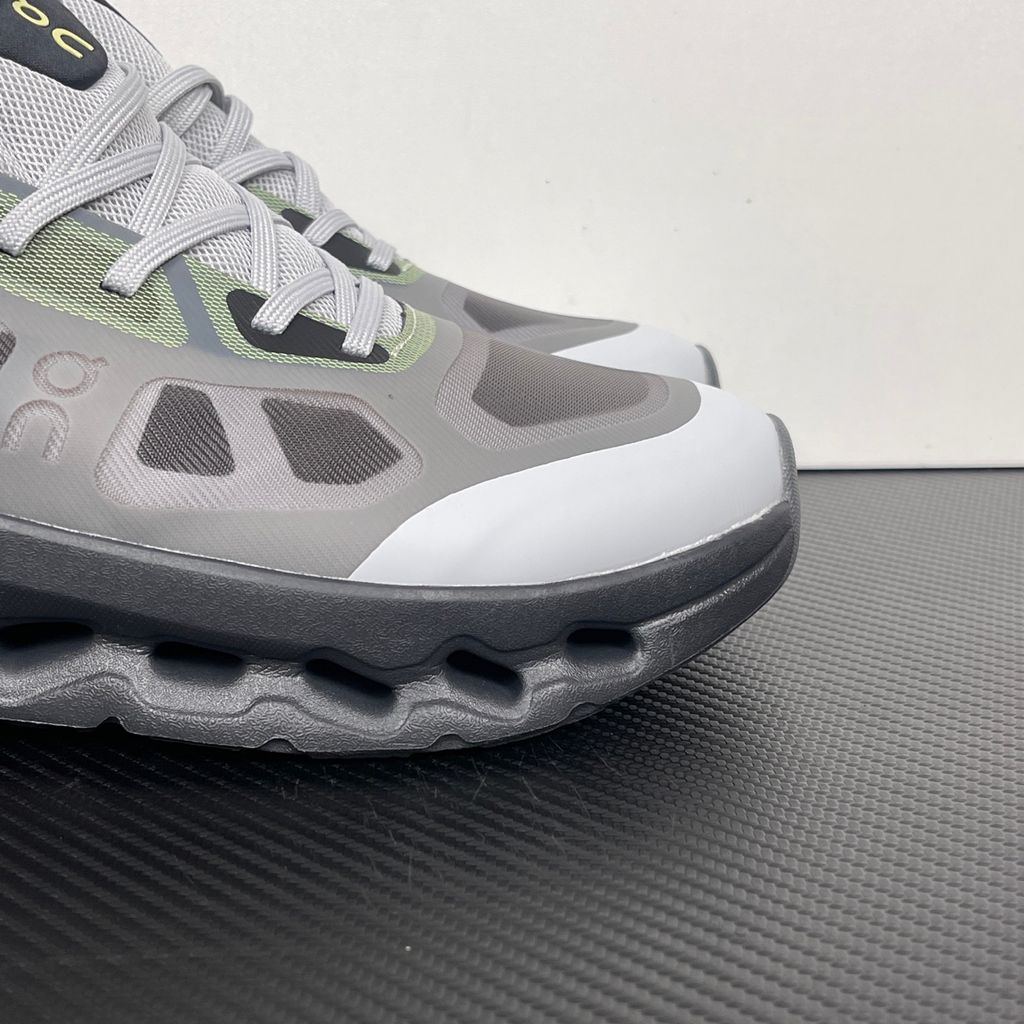 Side profile of the On Running Cloudtilt Remix sneaker, showcasing the mixed-material upper in dark grey and white with subtle green mesh undertones, quick-adjust speed lacing, and the distinctive dark grey CloudTec Phase® collapsing midsole.