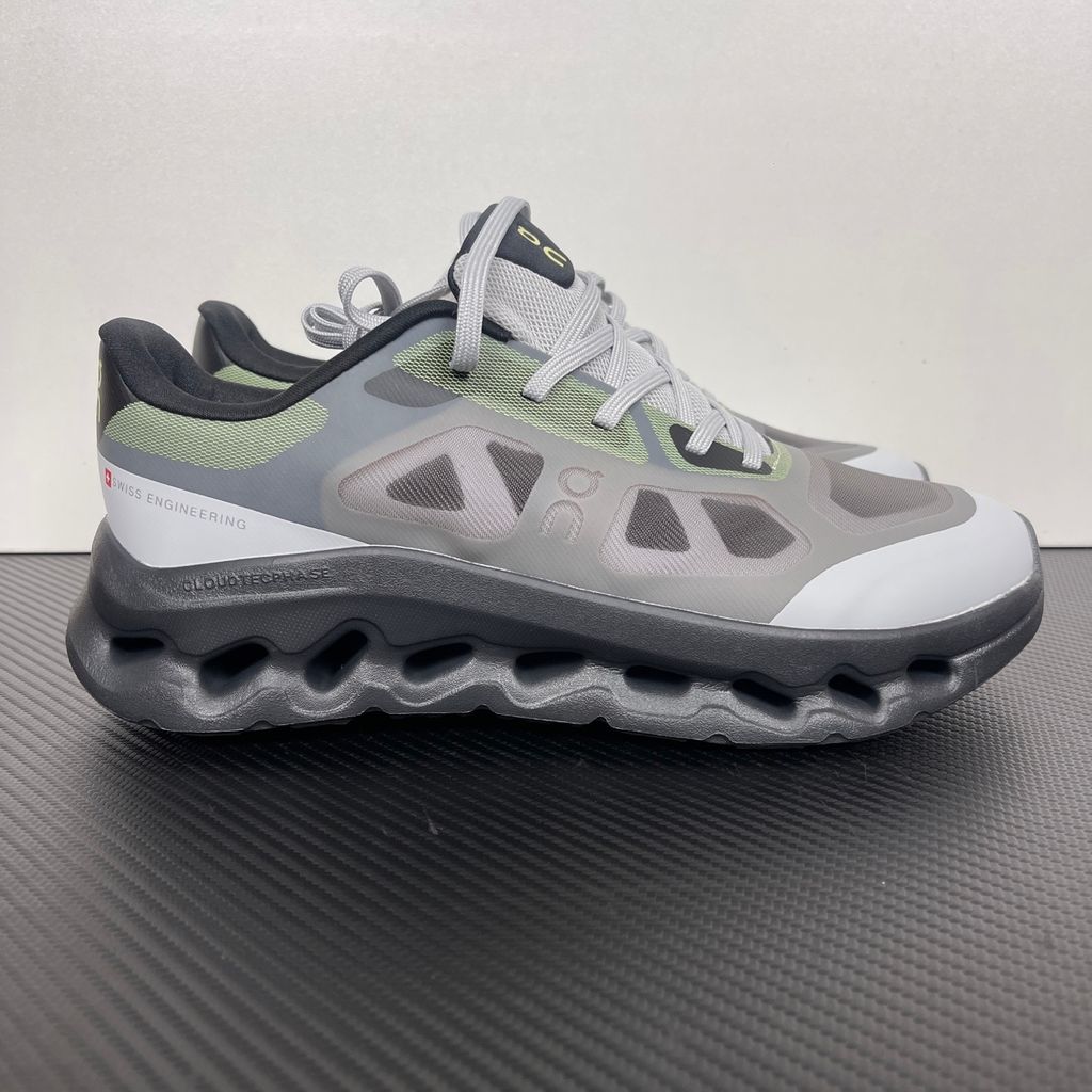Side profile of the On Running Cloudtilt Remix sneaker, showcasing the mixed-material upper in dark grey and white with subtle green mesh undertones, quick-adjust speed lacing, and the distinctive dark grey CloudTec Phase® collapsing midsole.