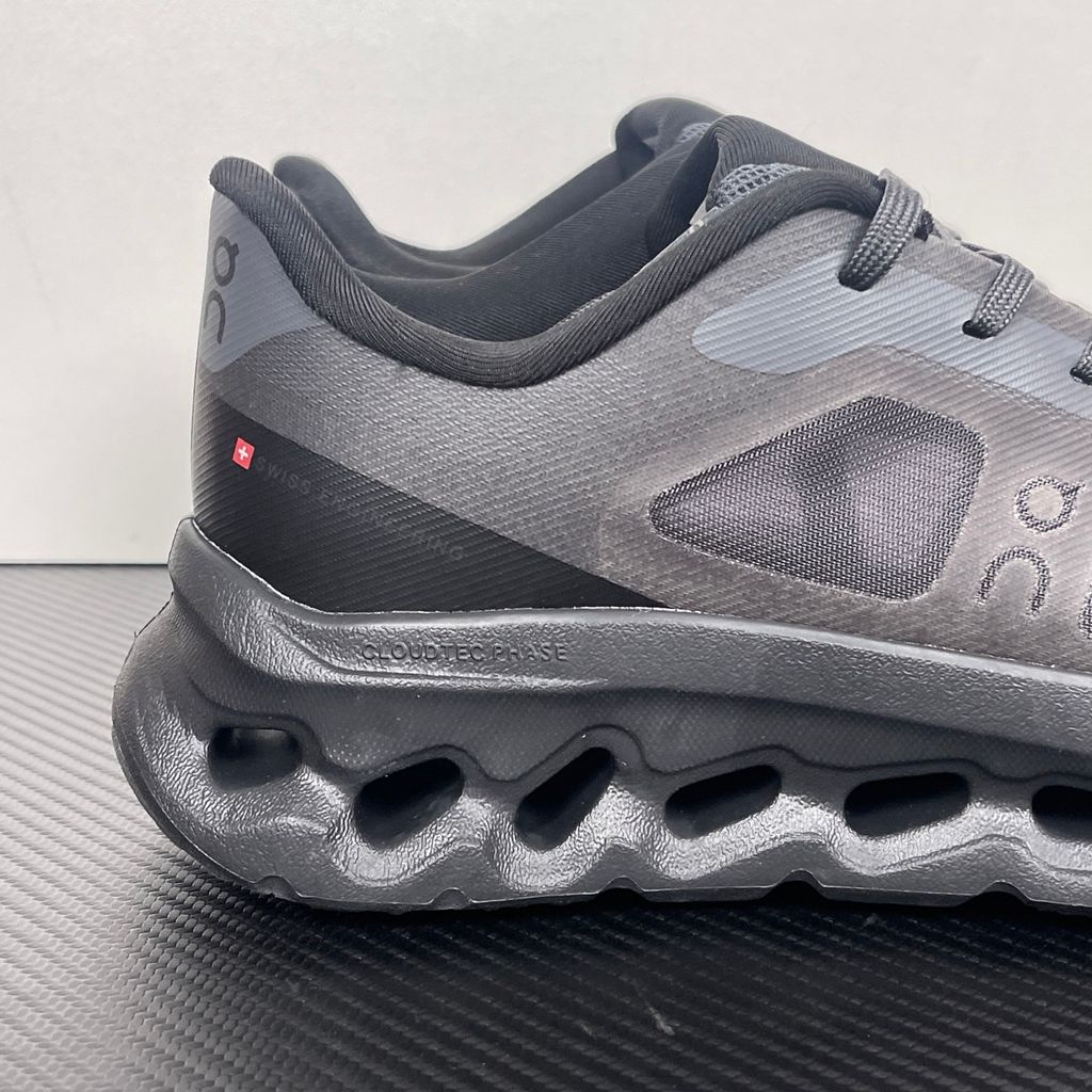 Side profile of the On Running Cloudtilt Remix sneaker in a monochromatic 'Triple Black' colorway, showcasing the mixed-material mesh and synthetic upper, quick-adjust speed lacing, and the stealthy black CloudTec Phase® collapsing midsole.