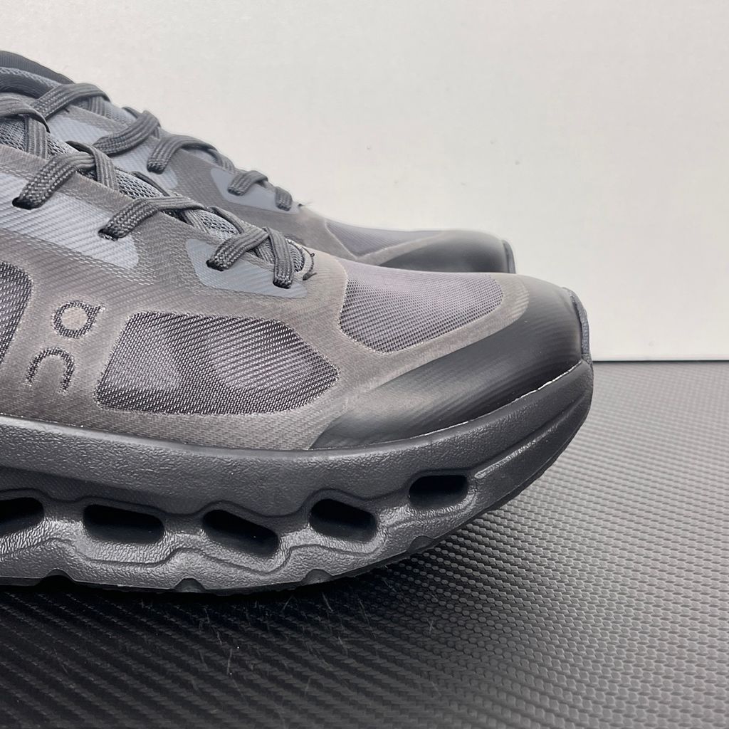 Side profile of the On Running Cloudtilt Remix sneaker in a monochromatic 'Triple Black' colorway, showcasing the mixed-material mesh and synthetic upper, quick-adjust speed lacing, and the stealthy black CloudTec Phase® collapsing midsole.