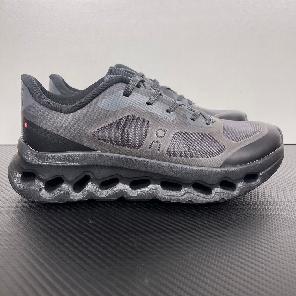 Side profile of the On Running Cloudtilt Remix sneaker in a monochromatic 'Triple Black' colorway, showcasing the mixed-material mesh and synthetic upper, quick-adjust speed lacing, and the stealthy black CloudTec Phase® collapsing midsole.