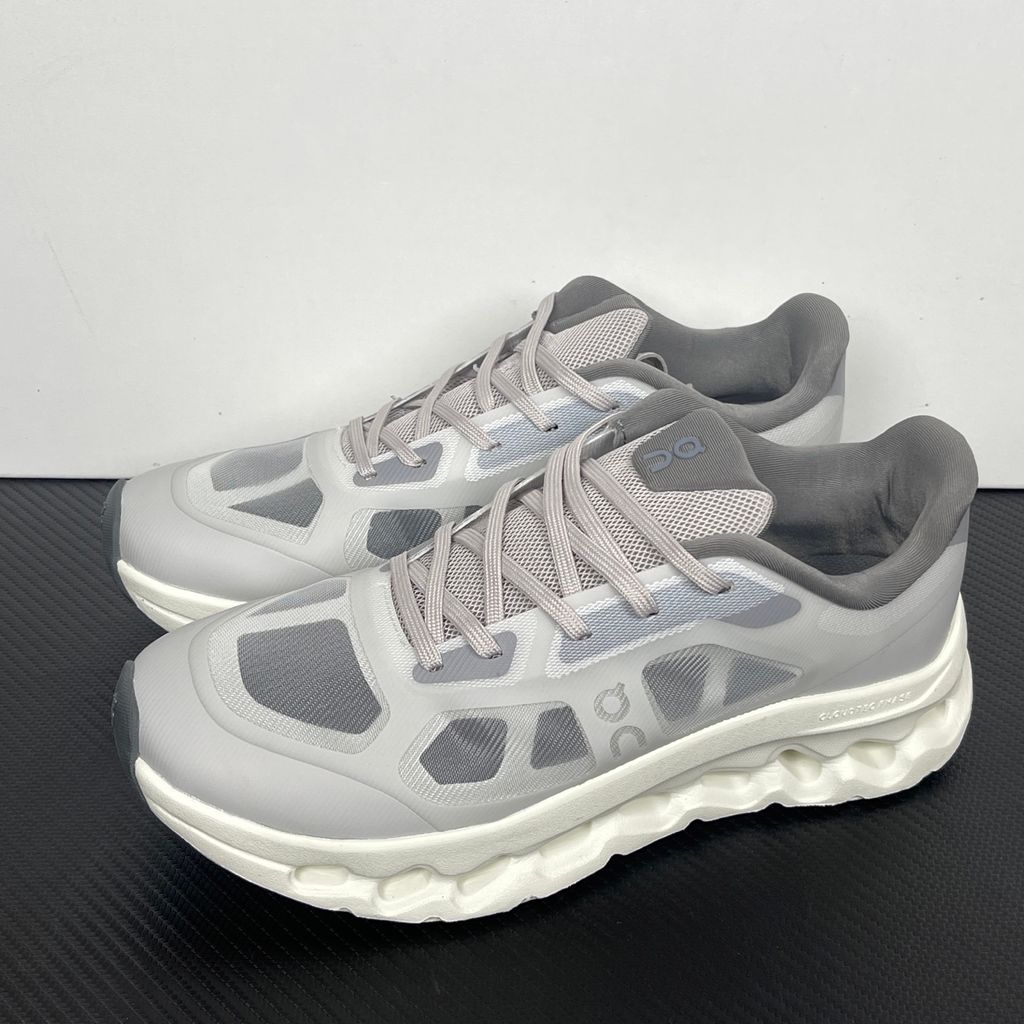 ide profile of the On Running Cloudtilt Remix sneaker, showcasing the mixed-material upper featuring a tonal grey breathable mesh base with matching grey synthetic overlays, speed lacing, and the distinctive white CloudTec Phase® collapsing midsole.