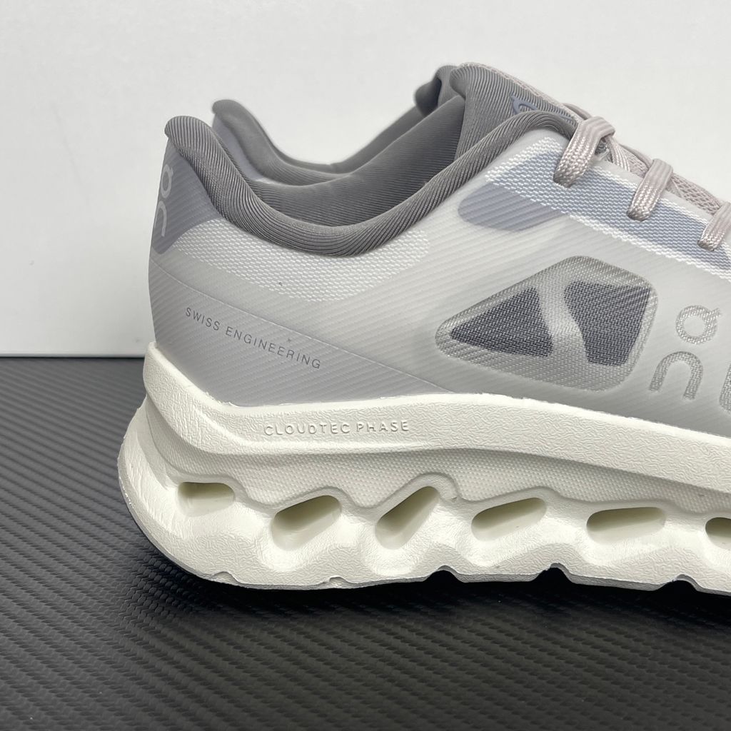 ide profile of the On Running Cloudtilt Remix sneaker, showcasing the mixed-material upper featuring a tonal grey breathable mesh base with matching grey synthetic overlays, speed lacing, and the distinctive white CloudTec Phase® collapsing midsole.