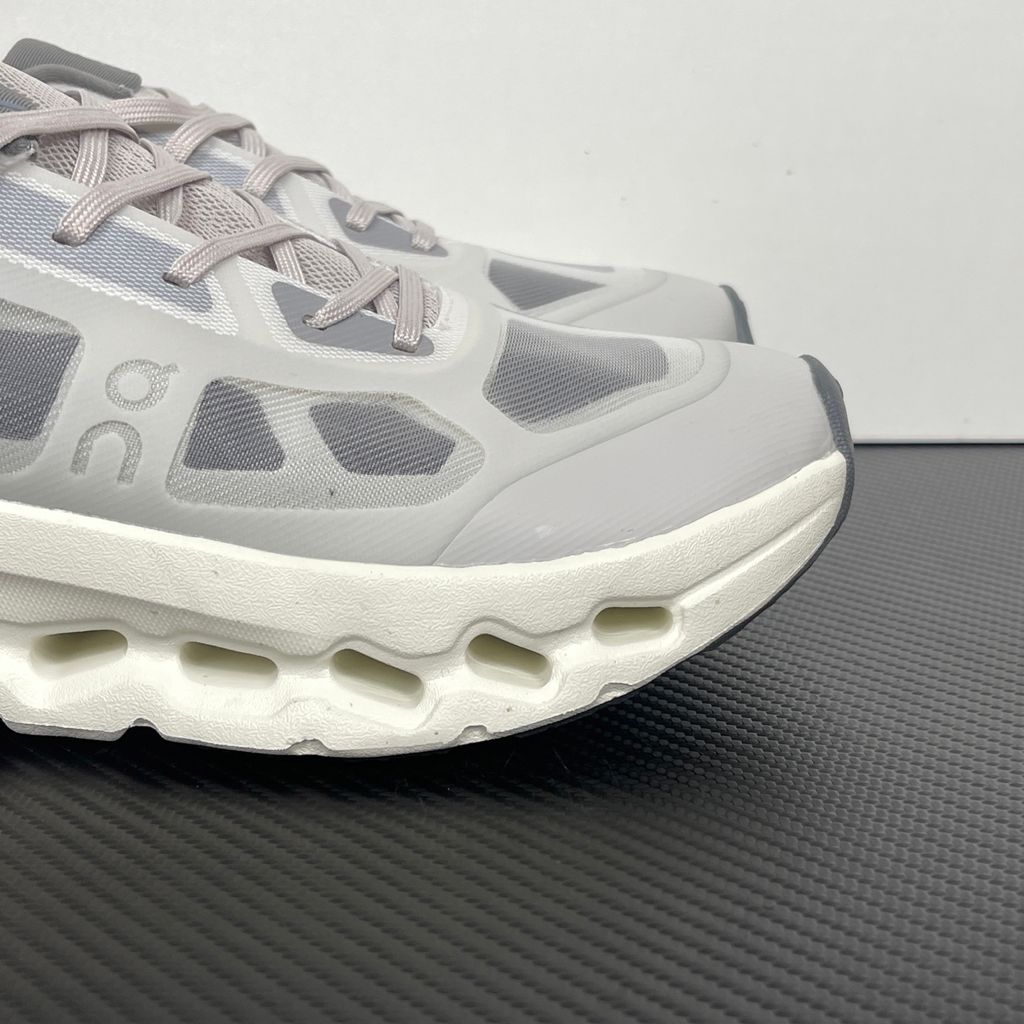 ide profile of the On Running Cloudtilt Remix sneaker, showcasing the mixed-material upper featuring a tonal grey breathable mesh base with matching grey synthetic overlays, speed lacing, and the distinctive white CloudTec Phase® collapsing midsole.