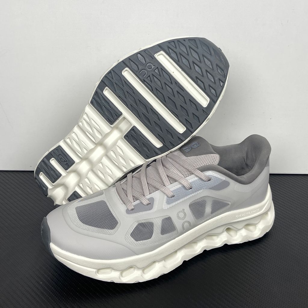 ide profile of the On Running Cloudtilt Remix sneaker, showcasing the mixed-material upper featuring a tonal grey breathable mesh base with matching grey synthetic overlays, speed lacing, and the distinctive white CloudTec Phase® collapsing midsole.