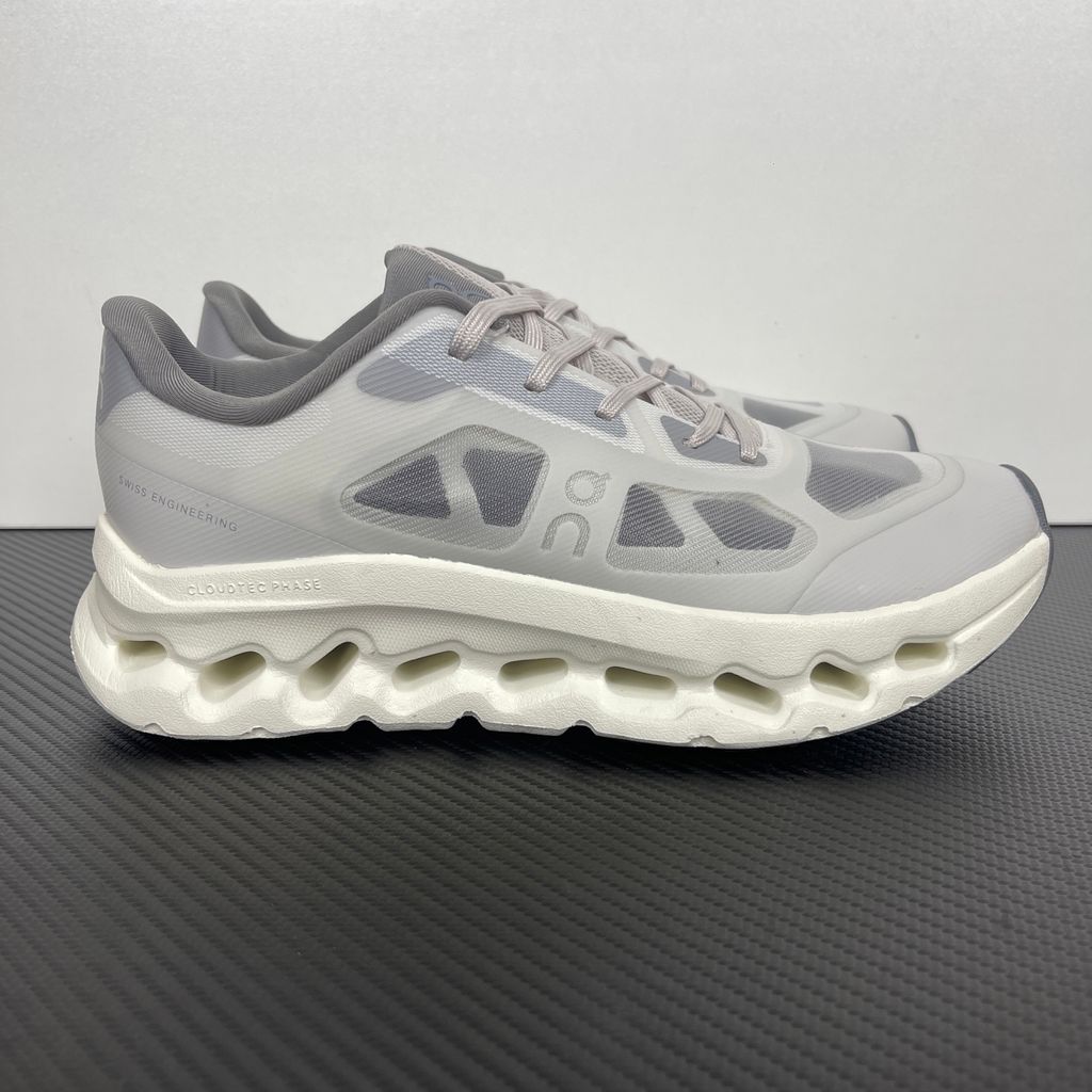 ide profile of the On Running Cloudtilt Remix sneaker, showcasing the mixed-material upper featuring a tonal grey breathable mesh base with matching grey synthetic overlays, speed lacing, and the distinctive white CloudTec Phase® collapsing midsole.
