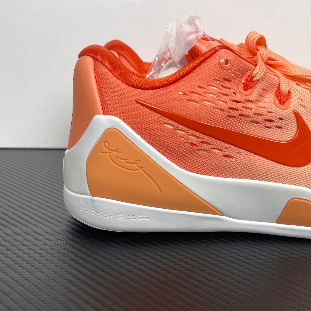 Side profile of the Nike Kobe 9 EM Low Protro, showcasing the vibrant orange Engineered Mesh upper, black Nike Swoosh, carbon fiber heel counter, and the signature pressure-mapped traction pattern on the outsole.