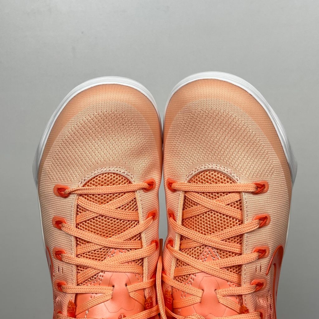 Side profile of the Nike Kobe 9 EM Low Protro, showcasing the vibrant orange Engineered Mesh upper, black Nike Swoosh, carbon fiber heel counter, and the signature pressure-mapped traction pattern on the outsole.