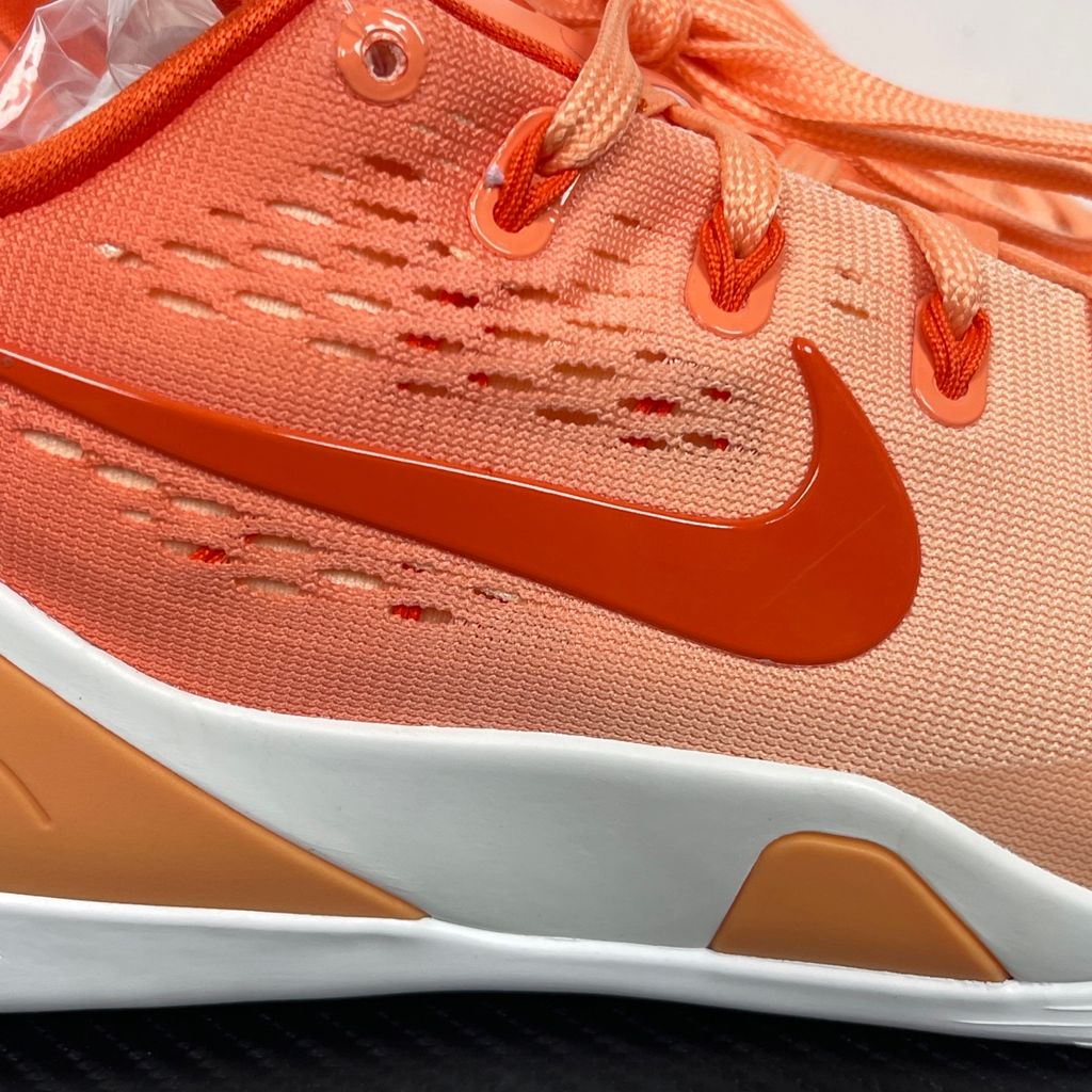 Side profile of the Nike Kobe 9 EM Low Protro, showcasing the vibrant orange Engineered Mesh upper, black Nike Swoosh, carbon fiber heel counter, and the signature pressure-mapped traction pattern on the outsole.