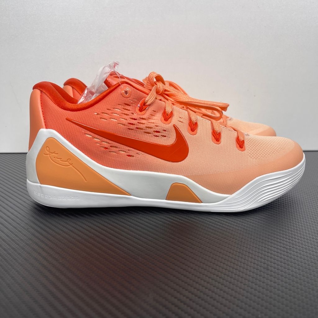 Side profile of the Nike Kobe 9 EM Low Protro, showcasing the vibrant orange Engineered Mesh upper, black Nike Swoosh, carbon fiber heel counter, and the signature pressure-mapped traction pattern on the outsole.