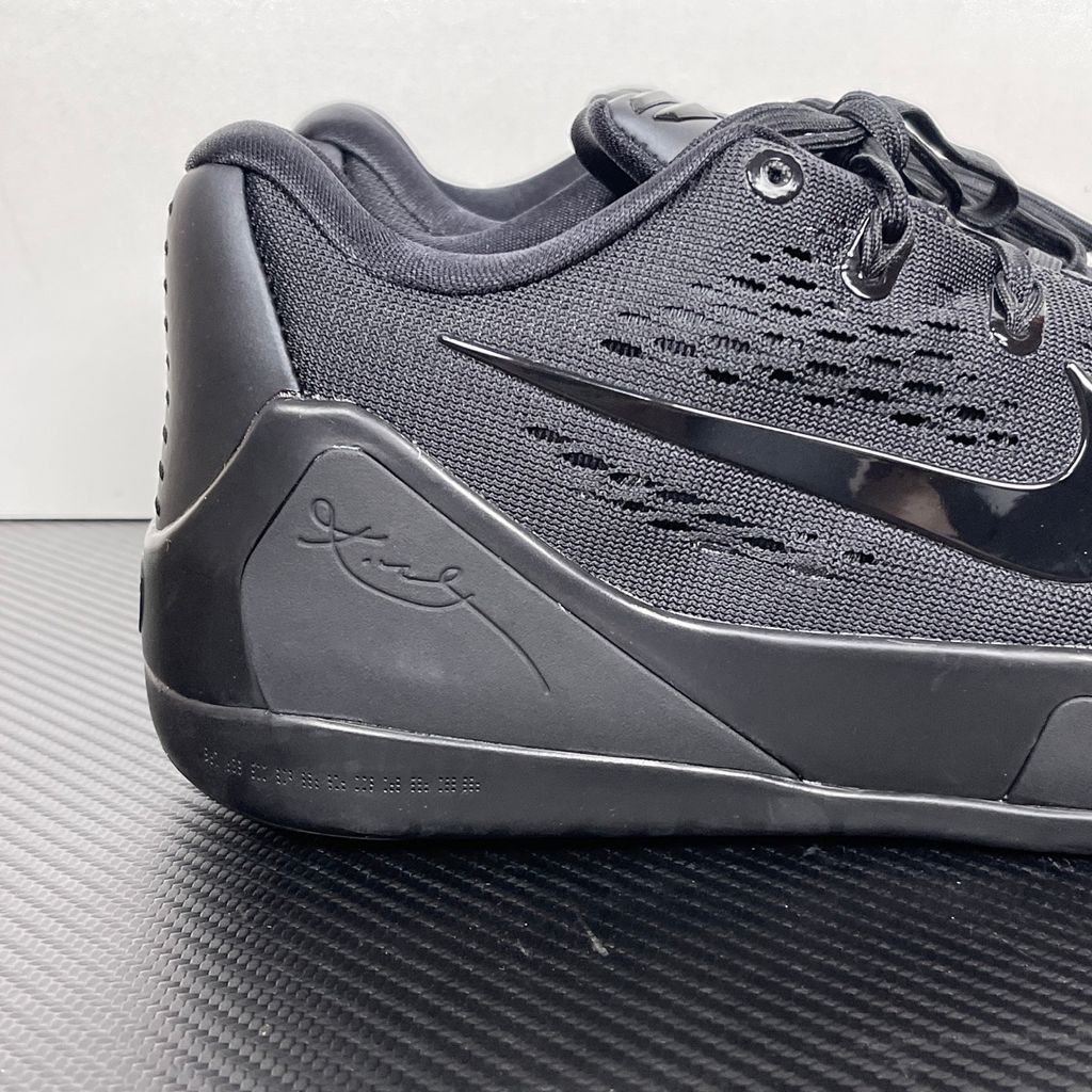 Side profile of the Nike Kobe 9 EM Low Protro TB sneaker in a monochromatic 'Triple Black' colorway, showcasing the stealthy Engineered Mesh upper, tonal black Swoosh, carbon fiber heel counter, and the signature black pressure-mapped outsole.