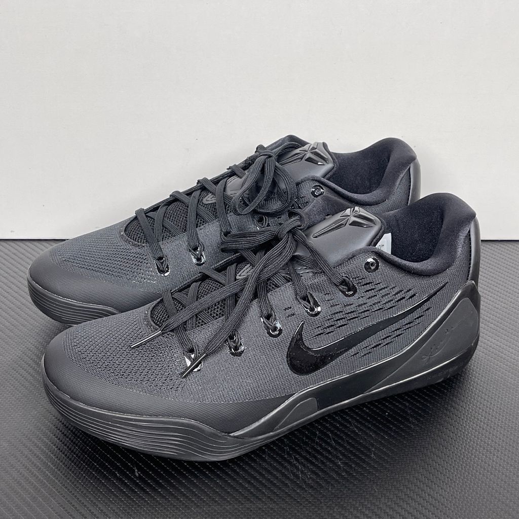 Side profile of the Nike Kobe 9 EM Low Protro TB sneaker in a monochromatic 'Triple Black' colorway, showcasing the stealthy Engineered Mesh upper, tonal black Swoosh, carbon fiber heel counter, and the signature black pressure-mapped outsole.