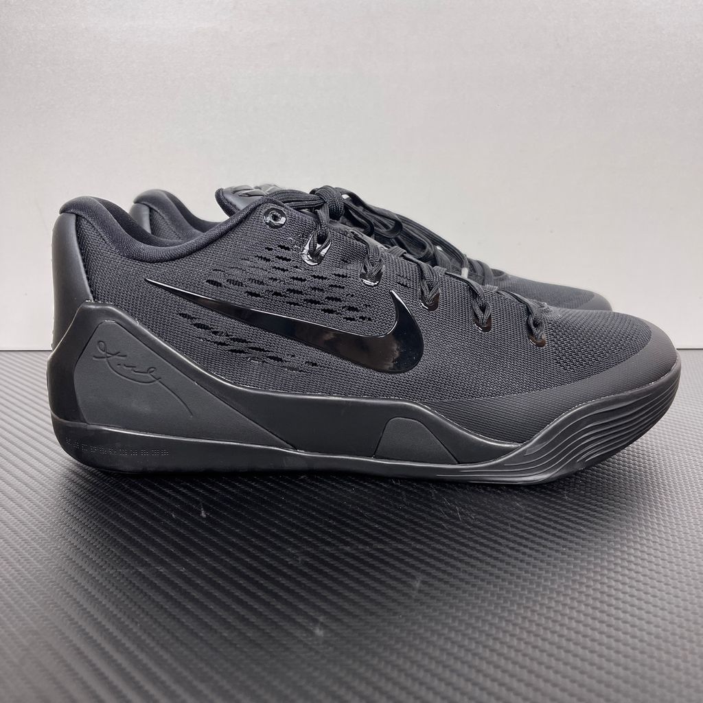 Side profile of the Nike Kobe 9 EM Low Protro TB sneaker in a monochromatic 'Triple Black' colorway, showcasing the stealthy Engineered Mesh upper, tonal black Swoosh, carbon fiber heel counter, and the signature black pressure-mapped outsole.