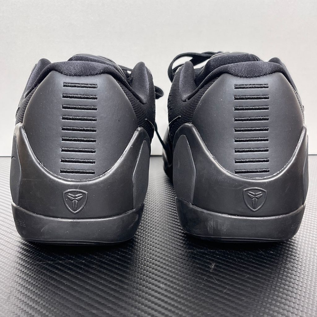 Side profile of the Nike Kobe 9 EM Low Protro TB sneaker in a monochromatic 'Triple Black' colorway, showcasing the stealthy Engineered Mesh upper, tonal black Swoosh, carbon fiber heel counter, and the signature black pressure-mapped outsole.