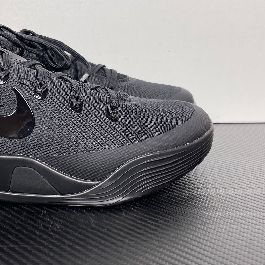 Side profile of the Nike Kobe 9 EM Low Protro TB sneaker in a monochromatic 'Triple Black' colorway, showcasing the stealthy Engineered Mesh upper, tonal black Swoosh, carbon fiber heel counter, and the signature black pressure-mapped outsole.