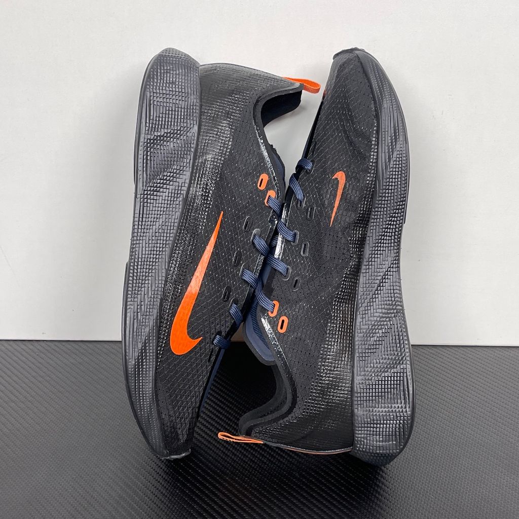 Side profile of the Nike Ava X sneaker in the 'Dark Obsidian Bright Mandarin' colorway, showcasing a deep navy blue breathable mesh upper, vibrant orange contrasting Swoosh and synthetic overlays, and a sculpted, responsive foam midsole.
