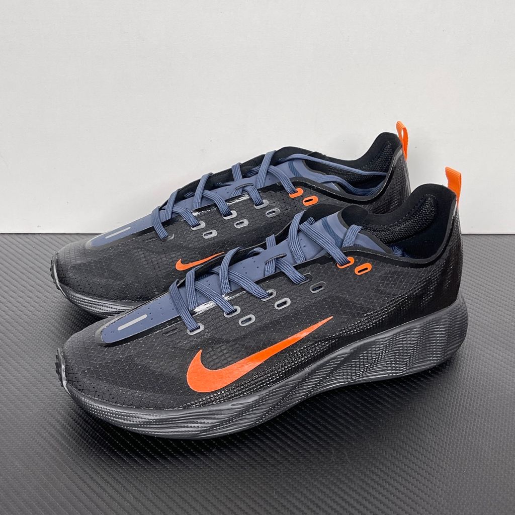Side profile of the Nike Ava X sneaker in the 'Dark Obsidian Bright Mandarin' colorway, showcasing a deep navy blue breathable mesh upper, vibrant orange contrasting Swoosh and synthetic overlays, and a sculpted, responsive foam midsole.
