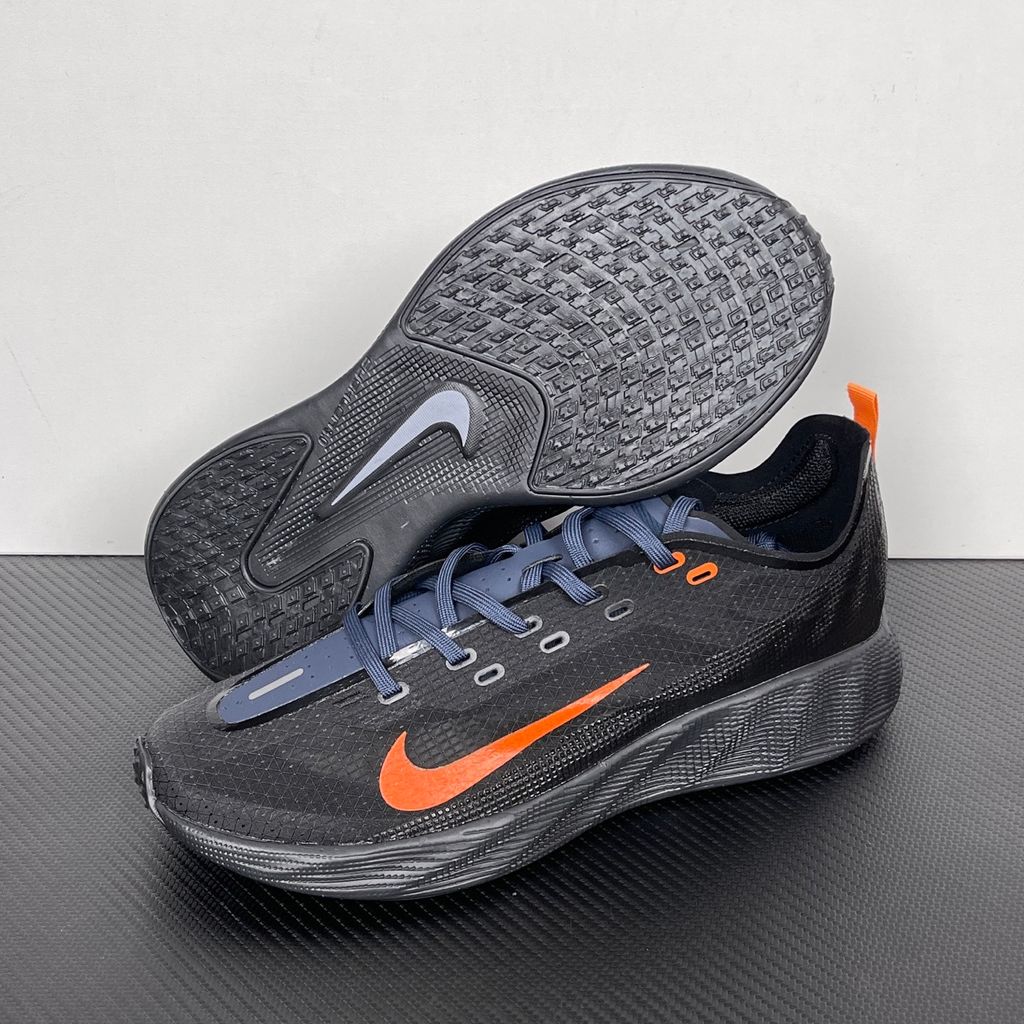 Side profile of the Nike Ava X sneaker in the 'Dark Obsidian Bright Mandarin' colorway, showcasing a deep navy blue breathable mesh upper, vibrant orange contrasting Swoosh and synthetic overlays, and a sculpted, responsive foam midsole.