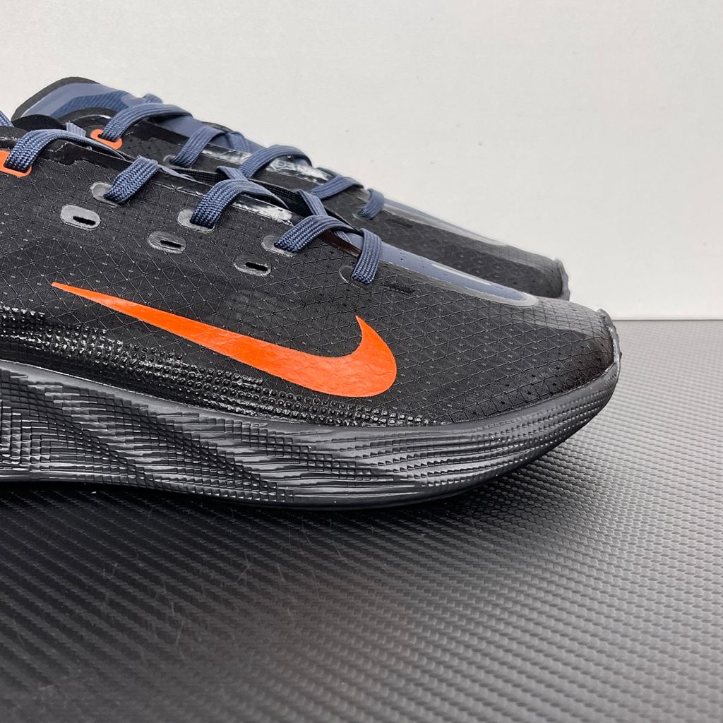 Side profile of the Nike Ava X sneaker in the 'Dark Obsidian Bright Mandarin' colorway, showcasing a deep navy blue breathable mesh upper, vibrant orange contrasting Swoosh and synthetic overlays, and a sculpted, responsive foam midsole.