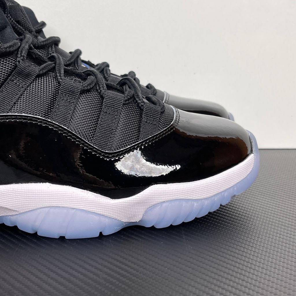 Side profile of the Air Jordan 11 Retro 'Space Jam' (2026), showcasing the high-gloss black patent leather mudguard, premium black mesh upper, white midsole, and the signature icy blue translucent outsole.