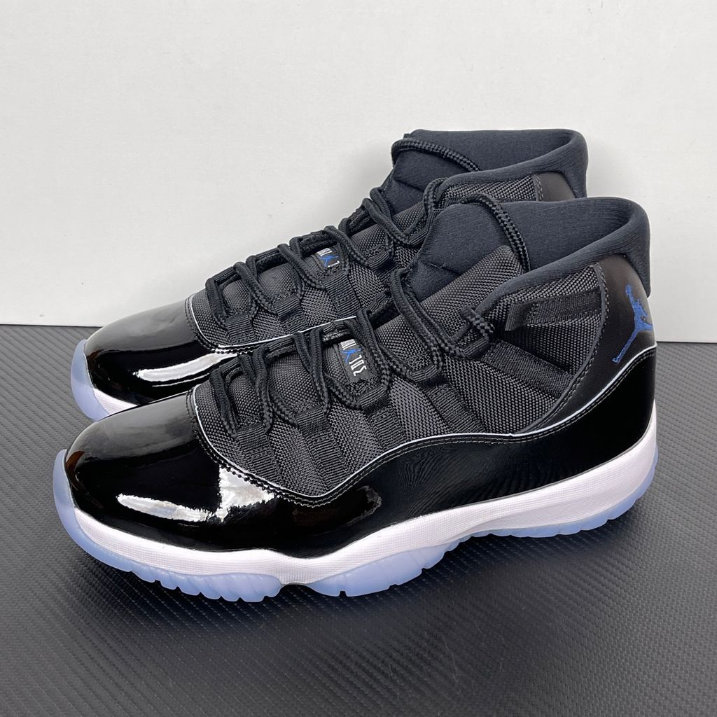 Side profile of the Air Jordan 11 Retro 'Space Jam' (2026), showcasing the high-gloss black patent leather mudguard, premium black mesh upper, white midsole, and the signature icy blue translucent outsole.
