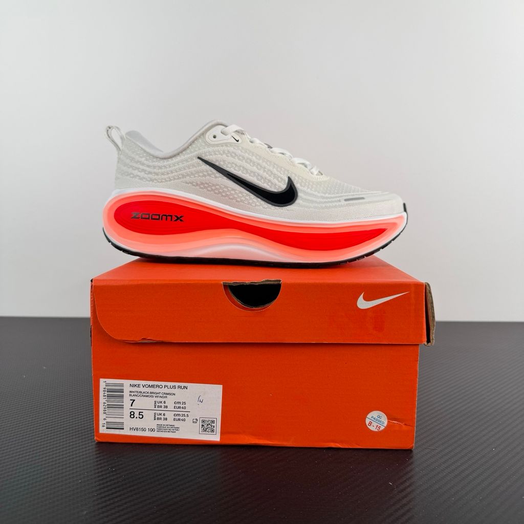 Side profile of the Nike Vomero Plus sneaker in the 'White Black Bright Crimson' colorway, showcasing the clean white mesh base, bold black synthetic overlays, and striking Bright Crimson accents on the midsole and branding.