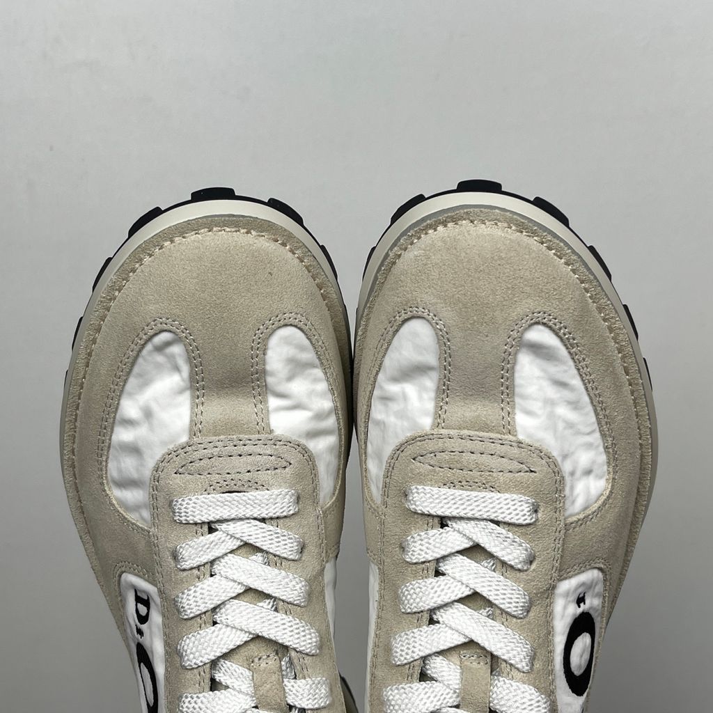 Side profile of the Dior Squash Sneaker, showcasing the white nylon base, beige suede overlays, prominent black "DiOr" side logo, and chunky white midsole with a black lugged outsole.