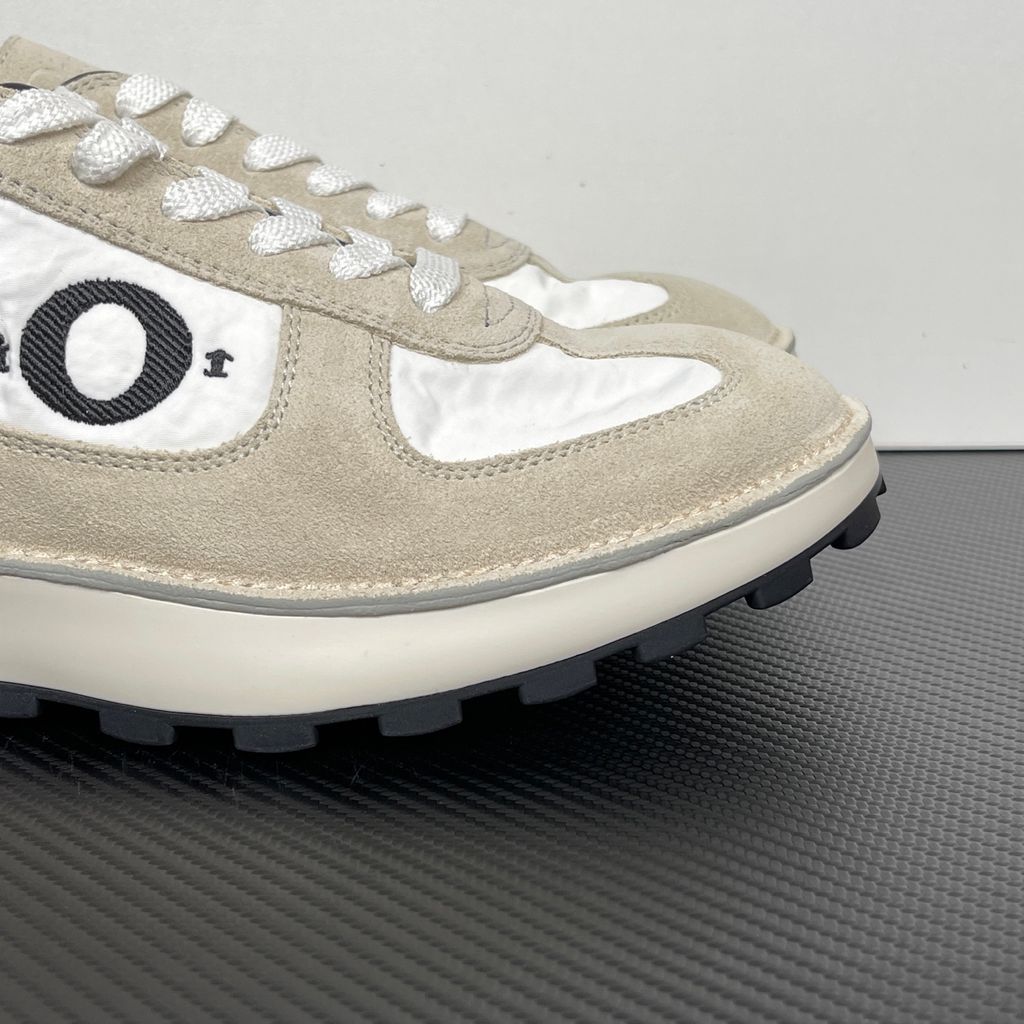 Side profile of the Dior Squash Sneaker, showcasing the white nylon base, beige suede overlays, prominent black "DiOr" side logo, and chunky white midsole with a black lugged outsole.