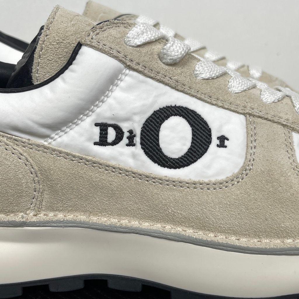 Side profile of the Dior Squash Sneaker, showcasing the white nylon base, beige suede overlays, prominent black "DiOr" side logo, and chunky white midsole with a black lugged outsole.