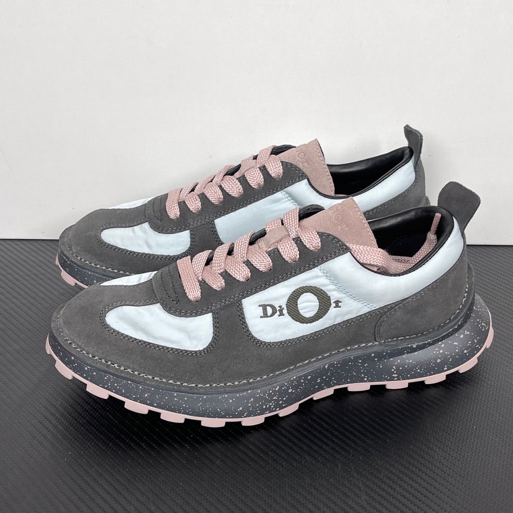 Side profile of the Dior Squash sneaker, highlighting the contrasting dark grey suede and light blue nylon upper, the unique 'DIOR' circular logo embroidery, and the speckled polyurethane midsole with a lugged outsole.