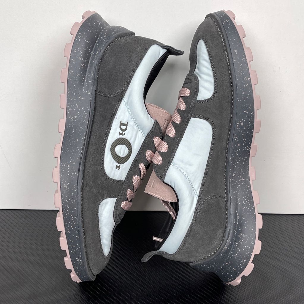 Side profile of the Dior Squash sneaker, highlighting the contrasting dark grey suede and light blue nylon upper, the unique 'DIOR' circular logo embroidery, and the speckled polyurethane midsole with a lugged outsole.