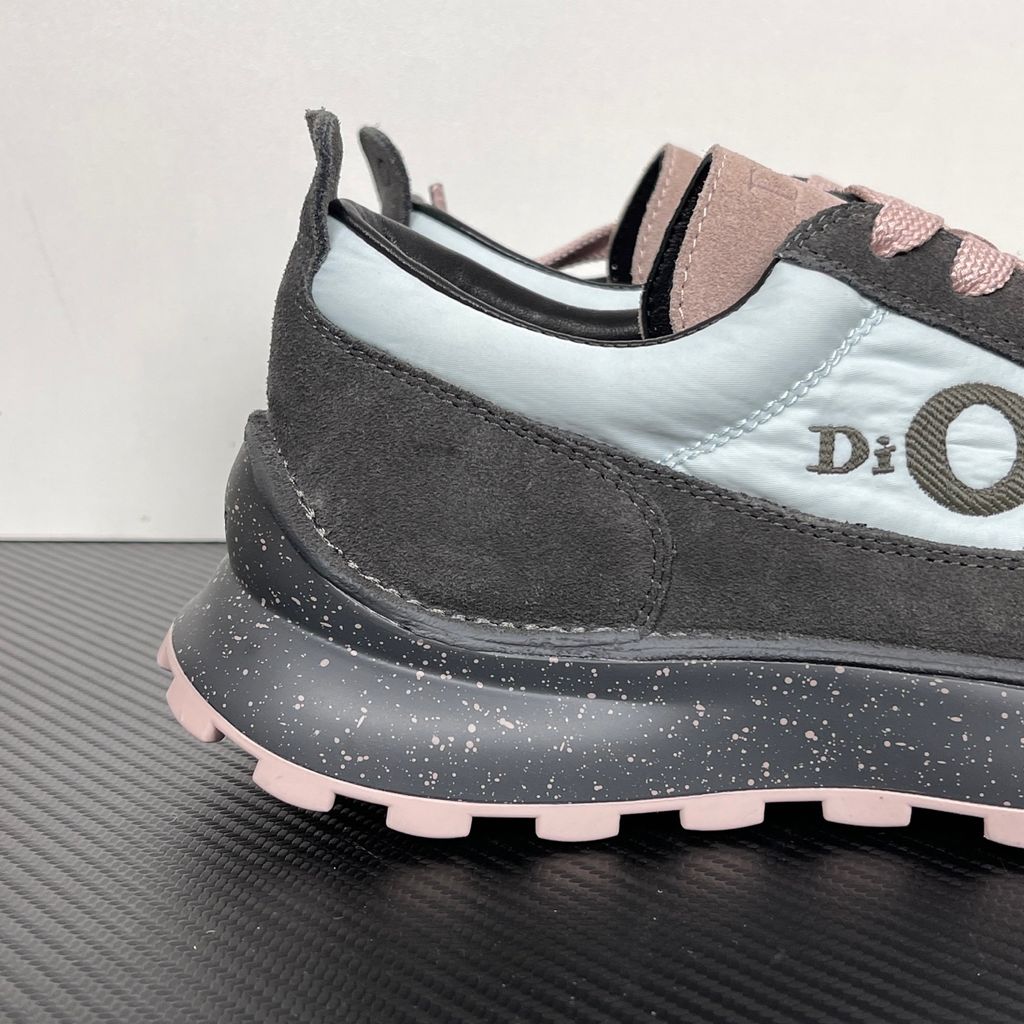 Side profile of the Dior Squash sneaker, highlighting the contrasting dark grey suede and light blue nylon upper, the unique 'DIOR' circular logo embroidery, and the speckled polyurethane midsole with a lugged outsole.