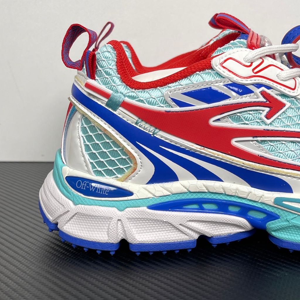 Side profile of the Off-White c/o Virgil Abloh sneaker showcasing a light blue mesh base, bold blue and red synthetic overlays, a large red arrow logo on the lateral side, and an attached blue and red zip-tie.