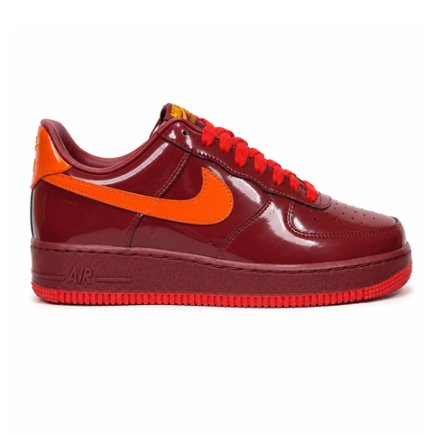 Side profile of the Nike Air Force 1 Low sneaker featuring a glossy Dark Team Red patent leather upper, striking Safety Orange accents on the signature Swoosh, and a classic white chunky midsole.