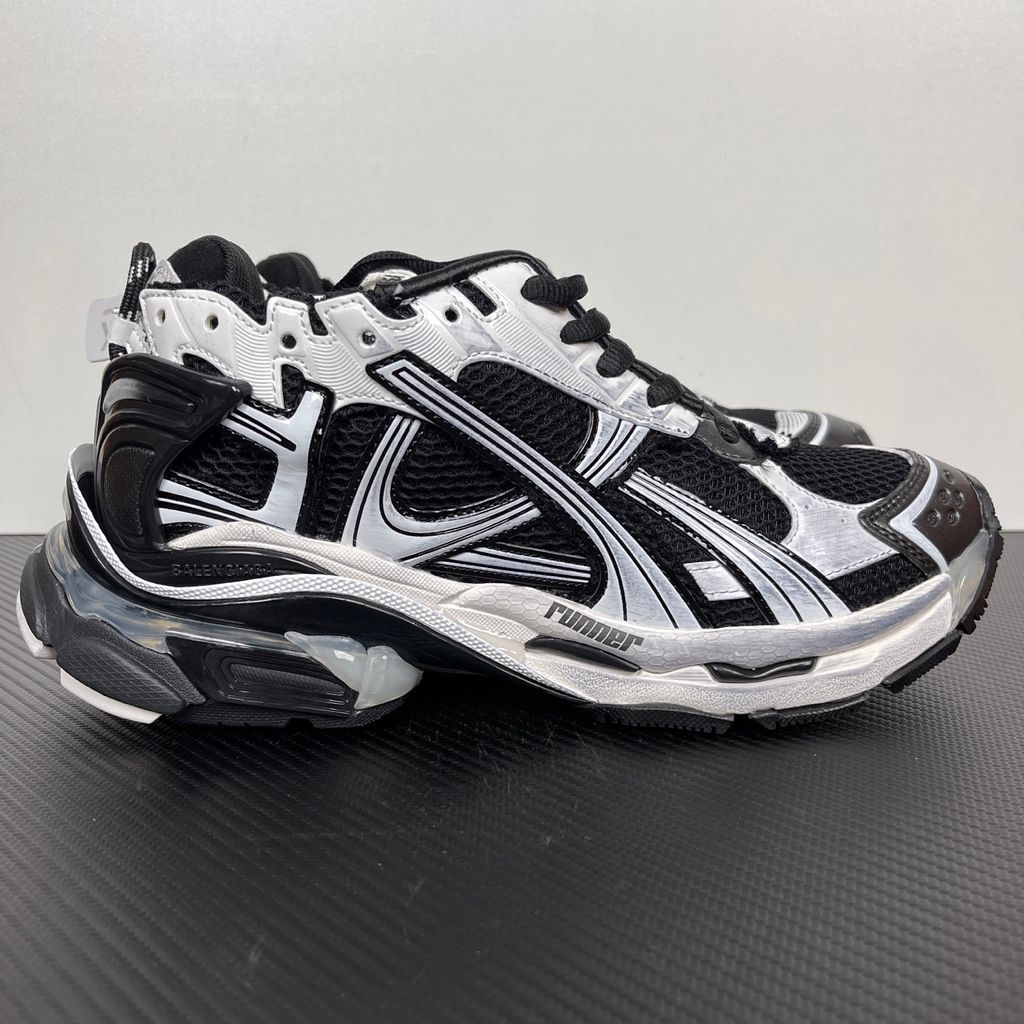 Side profile of the Balenciaga Runner LED sneaker in the 'Black/White' colorway, highlighting the intricate multi-layered mesh and synthetic construction, high-contrast paneling, and the clear heel capsule housing the LED technology.