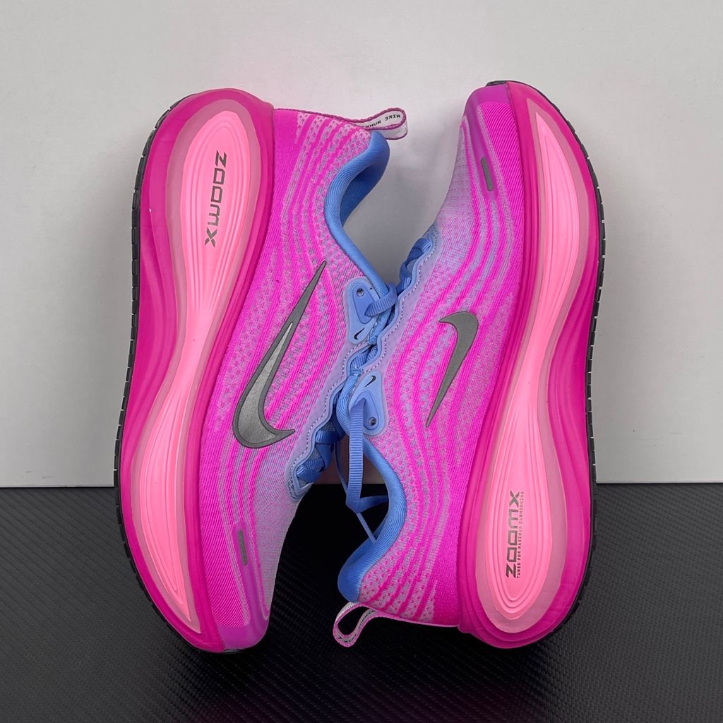 Side profile of the Nike Women's Vomero Plus running shoe, featuring a vibrant pink and purple engineered mesh upper, a metallic dark grey Swoosh, and a heavily cushioned, sculpted pink ZoomX foam midsole.