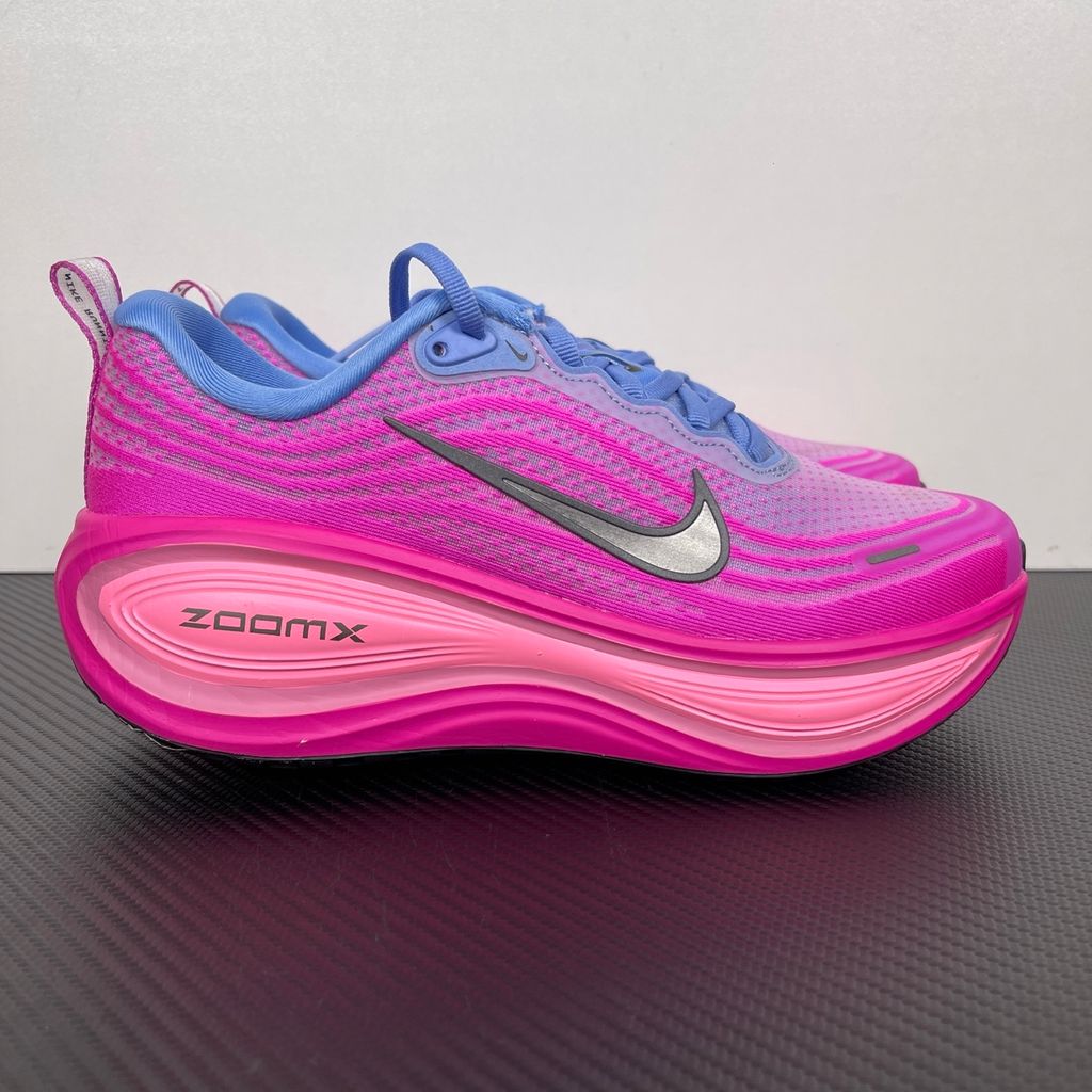 Side profile of the Nike Women's Vomero Plus running shoe, featuring a vibrant pink and purple engineered mesh upper, a metallic dark grey Swoosh, and a heavily cushioned, sculpted pink ZoomX foam midsole.