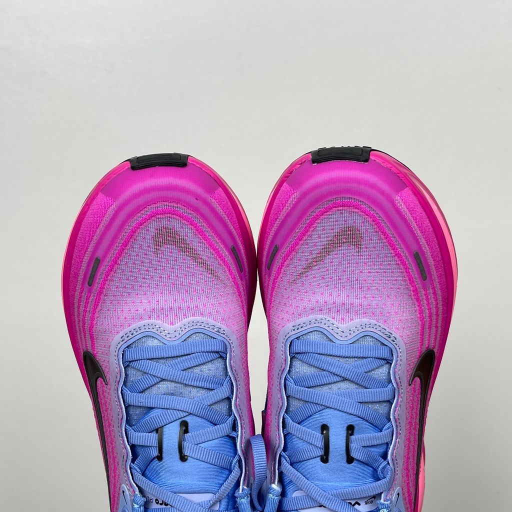 Side profile of the Nike Women's Vomero Plus running shoe, featuring a vibrant pink and purple engineered mesh upper, a metallic dark grey Swoosh, and a heavily cushioned, sculpted pink ZoomX foam midsole.