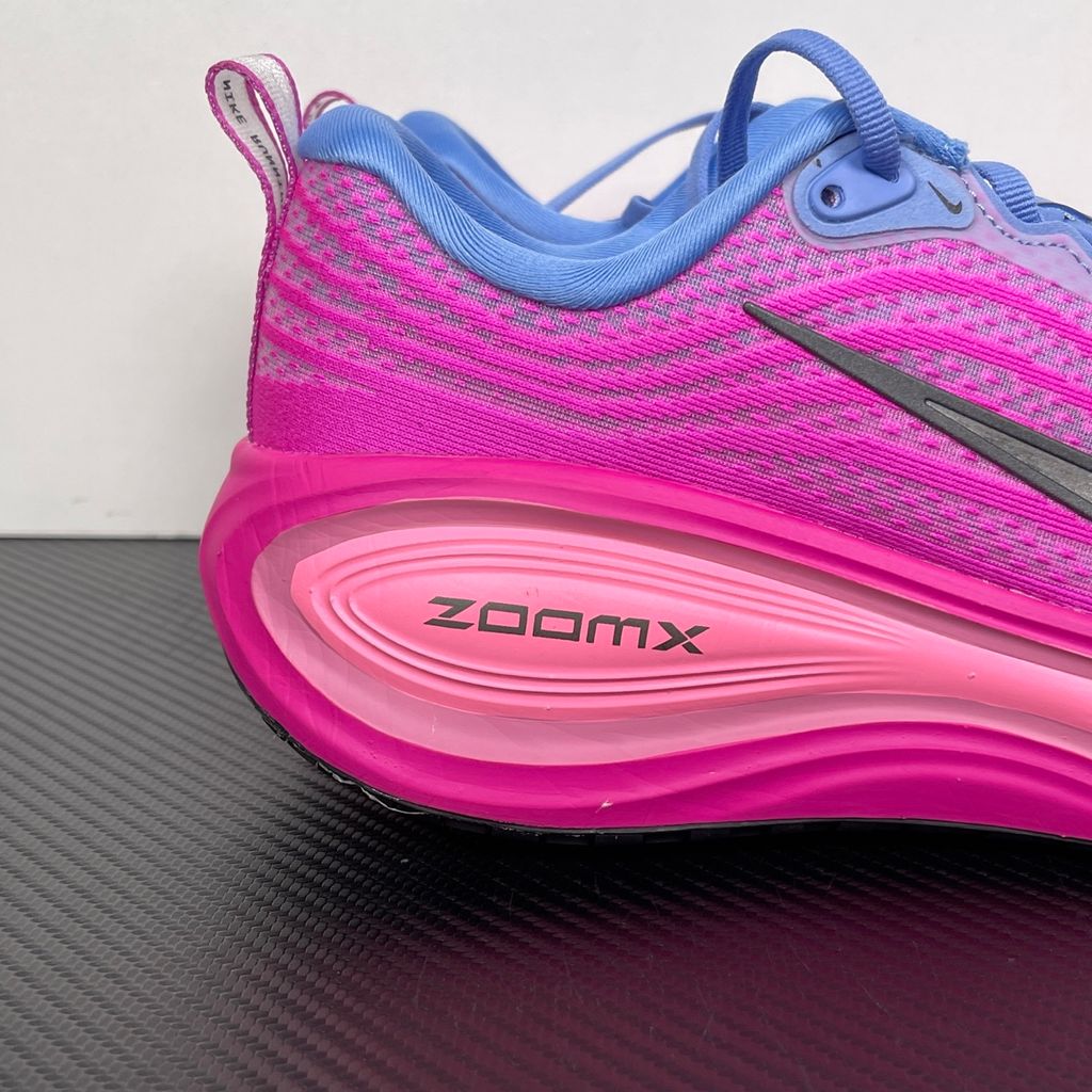 Side profile of the Nike Women's Vomero Plus running shoe, featuring a vibrant pink and purple engineered mesh upper, a metallic dark grey Swoosh, and a heavily cushioned, sculpted pink ZoomX foam midsole.
