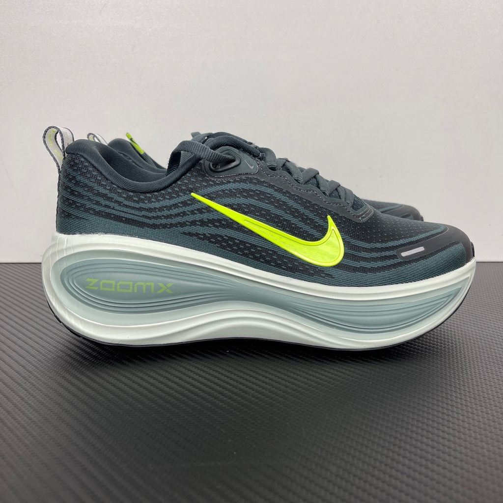 Side profile of the Nike Vomero Plus running shoe, featuring an earthy green engineered mesh upper with Seaweed and Cannon overlays, striking neon Volt accents, and a heavily cushioned, sculpted ZoomX foam midsole.