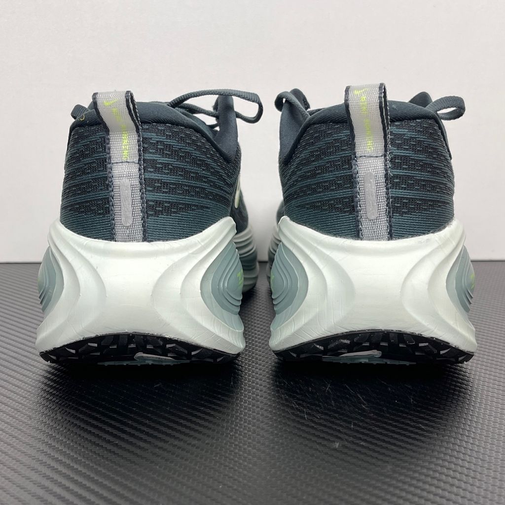 Side profile of the Nike Vomero Plus running shoe, featuring an earthy green engineered mesh upper with Seaweed and Cannon overlays, striking neon Volt accents, and a heavily cushioned, sculpted ZoomX foam midsole.