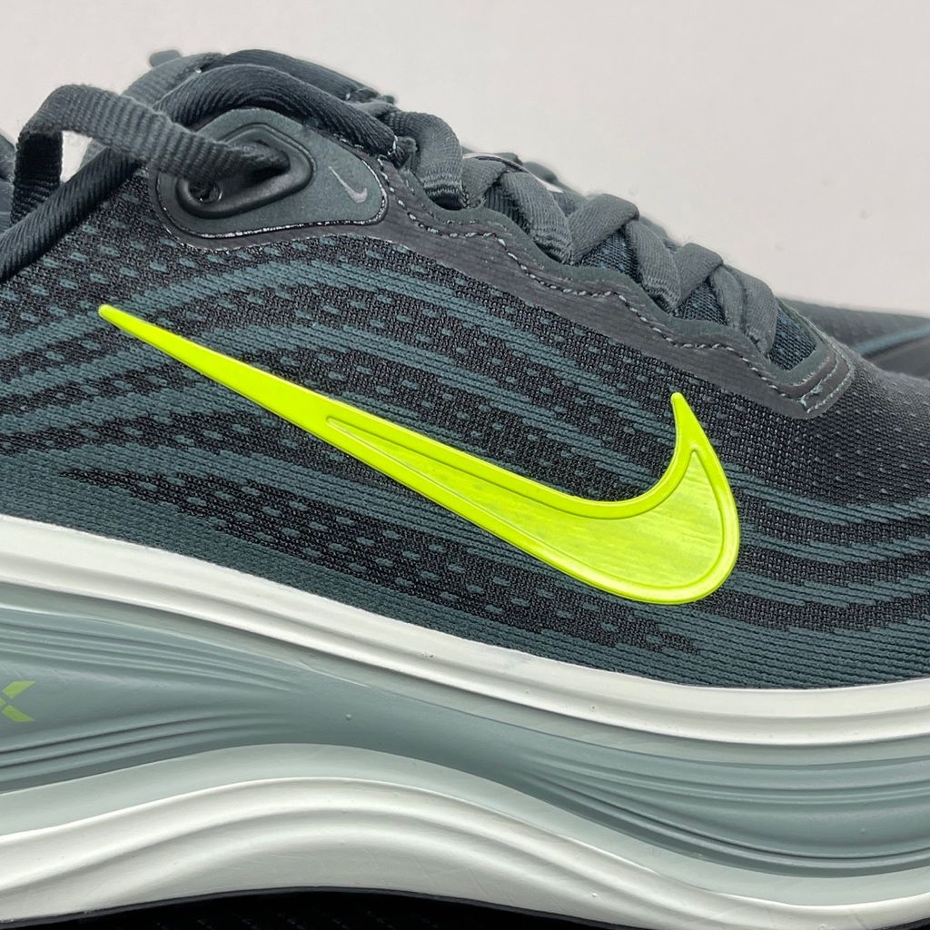 Side profile of the Nike Vomero Plus running shoe, featuring an earthy green engineered mesh upper with Seaweed and Cannon overlays, striking neon Volt accents, and a heavily cushioned, sculpted ZoomX foam midsole.