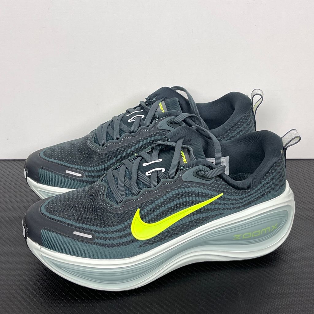 Side profile of the Nike Vomero Plus running shoe, featuring an earthy green engineered mesh upper with Seaweed and Cannon overlays, striking neon Volt accents, and a heavily cushioned, sculpted ZoomX foam midsole.
