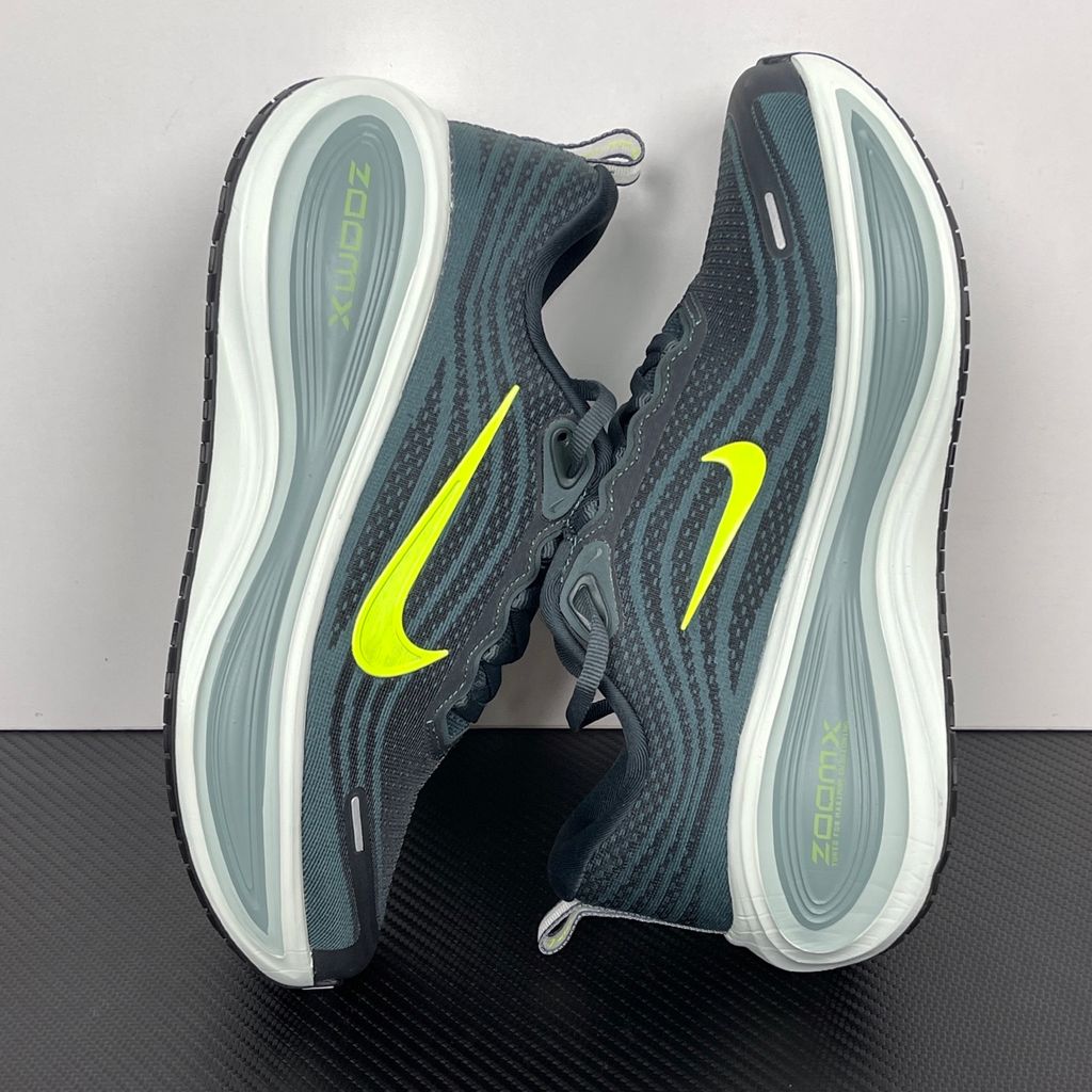 Side profile of the Nike Vomero Plus running shoe, featuring an earthy green engineered mesh upper with Seaweed and Cannon overlays, striking neon Volt accents, and a heavily cushioned, sculpted ZoomX foam midsole.