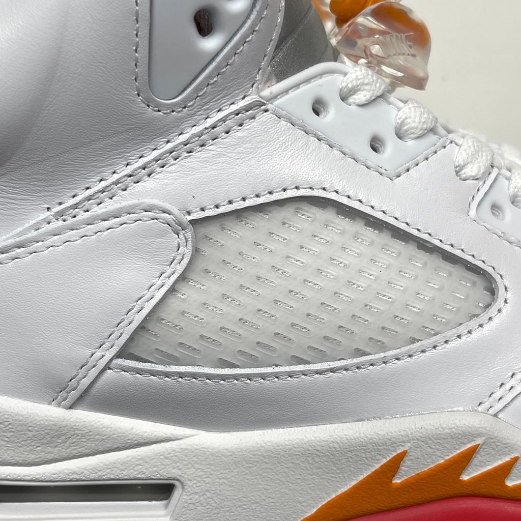 Side profile of the Air Jordan 5 Retro sneaker in the 'Sunset' colorway, featuring a crisp leather upper, vibrant orange and red sunset gradient accents, signature translucent netting, and the iconic shark tooth midsole detailing.