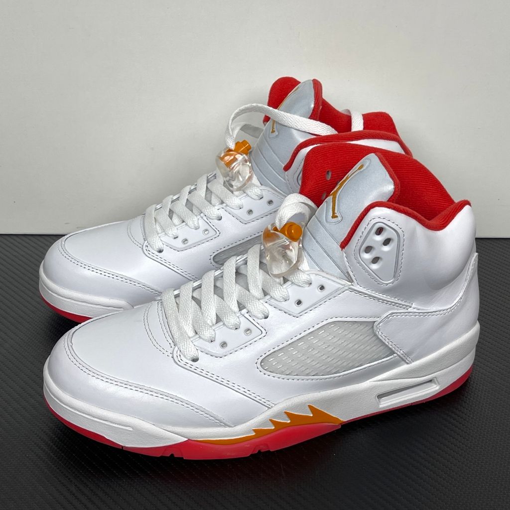 Side profile of the Air Jordan 5 Retro sneaker in the 'Sunset' colorway, featuring a crisp leather upper, vibrant orange and red sunset gradient accents, signature translucent netting, and the iconic shark tooth midsole detailing.