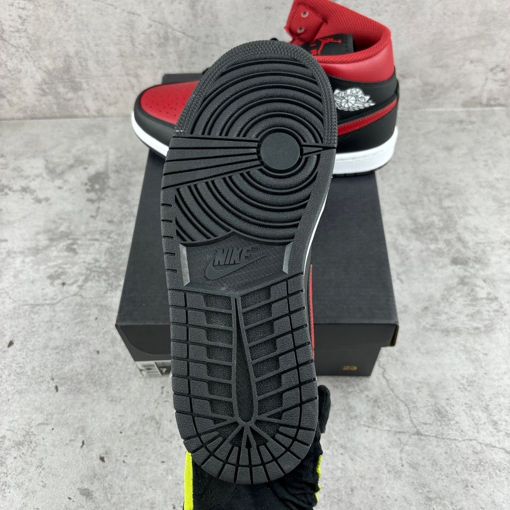 Side profile of the Air Jordan 1 Mid sneaker in the 'Bred Twist' colorway, featuring a crisp white leather base, bold black overlays, and vibrant University Red accents on the Swoosh, collar, and outsole.
