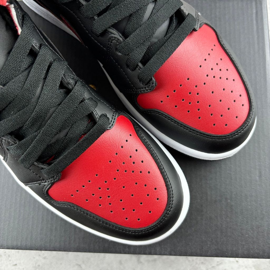 Side profile of the Air Jordan 1 Mid sneaker in the 'Bred Twist' colorway, featuring a crisp white leather base, bold black overlays, and vibrant University Red accents on the Swoosh, collar, and outsole.