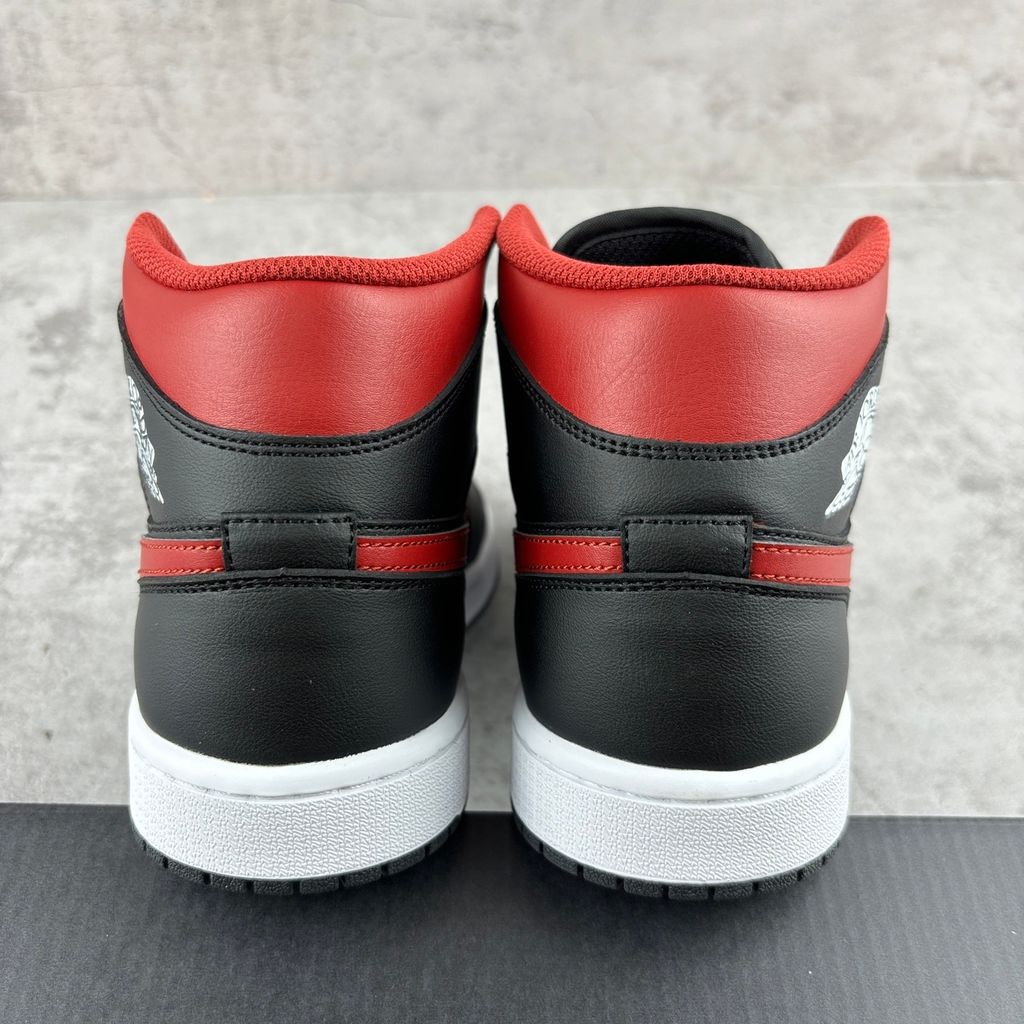 Side profile of the Air Jordan 1 Mid sneaker in the 'Bred Twist' colorway, featuring a crisp white leather base, bold black overlays, and vibrant University Red accents on the Swoosh, collar, and outsole.
